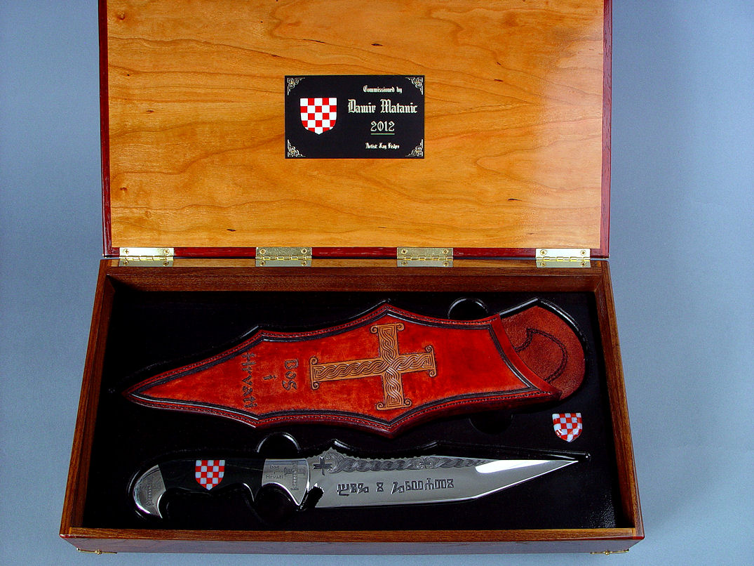"Duhovni Ratnik" cultural heritage knife. Knife in hand-engraved 440C high chromium stainless steel blade, hand-engraved 304 stainless steel bolsters, handle of Black Nephrite Jade gemstone inlaid with a mosaic of Red River Jasper and White Geodic Quartz. Sheath is hand-carved, hand-dyed leather shoulder