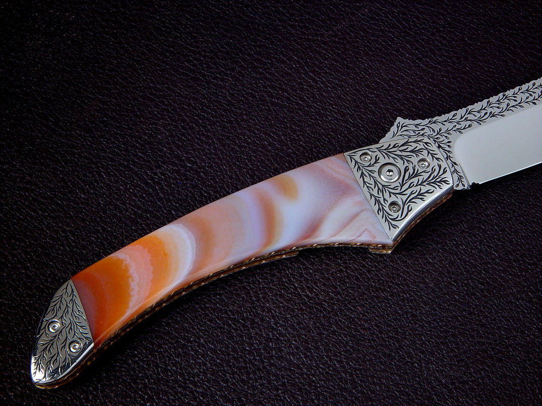 Heat treated Brazilian Agate on this "Procyon" reverse side view in hand-engraved 440C high chromium stainless steel blade, hand-engraved 304 stainless steel bolsters, anodized 6AL4V titanium liners and lock, polished Brazilian Agate gemstone handle, breccia marble case