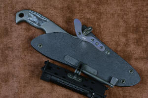 "Contego" Counterterrorism Tactical Knife, sheathed view, with HULA articulation outward and back, lock tab down, in T3 cryogenically treated CPM154CM  powder metal technology high molybdenum martensitic stainless steel blade, 304 stainless steel bolsters, Black/Gray G10 fiberglass/epoxy composite handle, hybrid tension tab-locking sheath in kydex, anodized aluminum, stainless steel, titanium