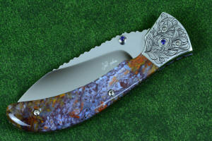 Macro enlargement of "Starling" fine handmade custom folding knife, obverse side view in high molybdenum stainless steel blade, engraved stainless bolsters, faceted amethyst gemstone accents and Rio Grande Agate handle Macro enlargement of "Starling" fine handmade custom folding knife, obverse side view in high molybdenum stainless steel blade, engraved stainless bolsters, faceted amethyst gemstone accents and Rio Grande Agate handle